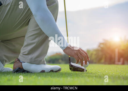 Man hand putting golf ball on tee in golf course - Image Stock Photo