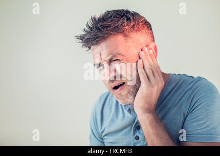 male having ear pain touching his painful head isolated on gray background Stock Photo