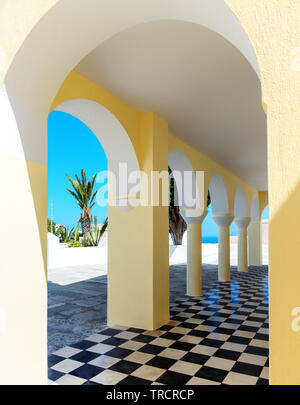 Church portico in Oia Santorini with butter yellow stucco arches contrasting against striking black and white tile floor. Stock Photo