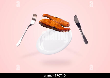 grilled salmon fish falling on the levitating plate, fork and knife. conceptual food background Stock Photo