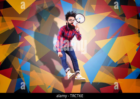 Bearded hipster man in glasses, jumping and shouting in megaphone, photo over colored background with geometric elements Stock Photo