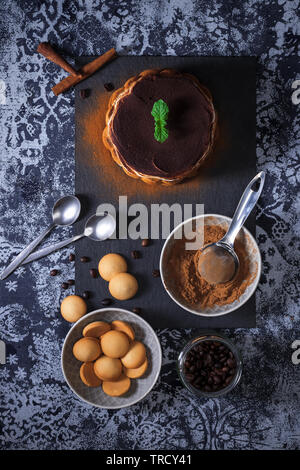 Round tiramisu, homemade no-bake chocolate dessert, traditional Italian sweet food. Table with cake, bowl with cocoa powder, round sponge biscuits, ja Stock Photo