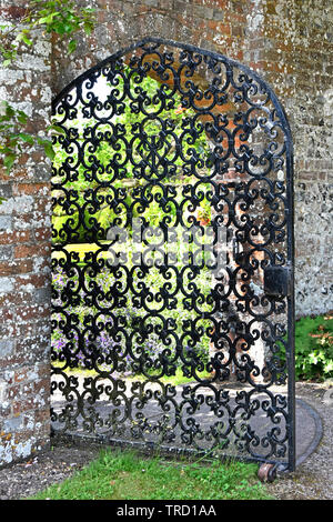 Old lockable heavy ornamental wrought iron gate on steel track open in arch brick wall opening giving access to walled garden country home England UK Stock Photo