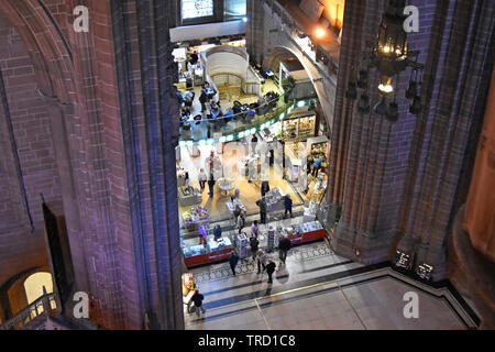 Looking down from high above on people shopping in gift shop & cafe inside nave of Liverpool Anglican cathedral with coloured wall lighting England UK Stock Photo