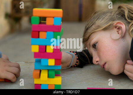 A child removes an orange wooden block from a tower with stacked wooden blocks. Stock Photo