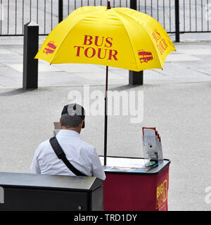 London street scene tourism tour bus salesman sitting on pavement at small desk under yellow advertising umbrella hot summer day Westminster Abbey UK Stock Photo