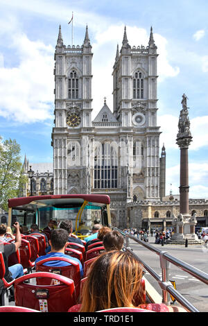 Open top double decker tourist bus passengers on summer sightseeing tour at west front Westminster Abbey with Scholars War Memorial column London UK Stock Photo