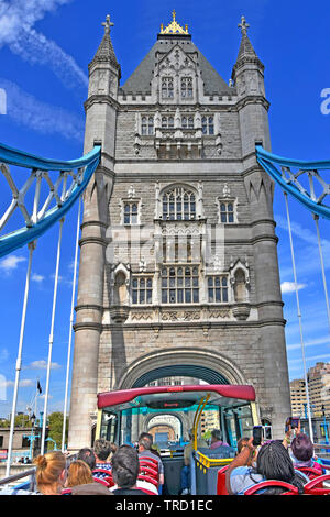Open top double decker tourist bus back view of passengers on summer sightseeing tour on Tower Bridge taking photos on blue sky day London England UK Stock Photo