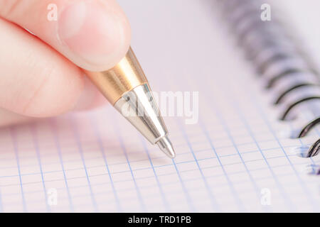 Teen writes black yellow pen in a checkered notebook. Spiral bound Stock Photo