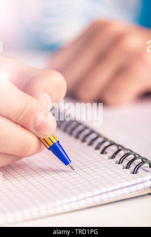 Teen writes black yellow pen in a checkered notebook. Spiral bound Stock Photo