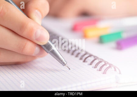 Teen writes black yellow pen in a checkered notebook. With colored markers Stock Photo