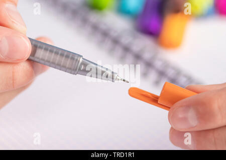 Unpacking orange felt-tip pen on the background of the notebook. In one hand case, in the other - the lid. Stock Photo