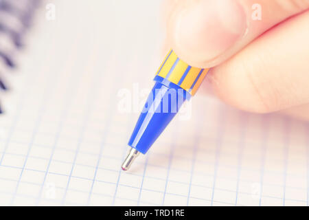 A man or teenager writes a blue-yellow pen in a checkered notebook. The concept of passing the exam and test Stock Photo