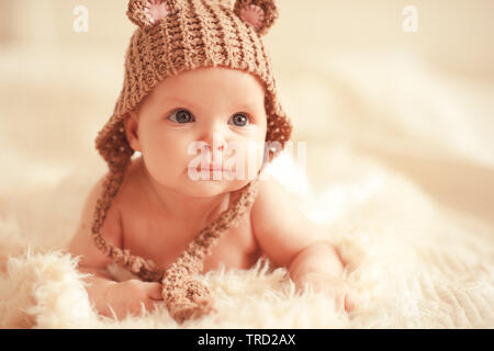 Cute baby girl wearing knitted hat lying in bed close up. Looking away. Childhood. Stock Photo