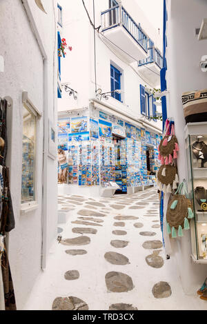 The cobble paved, narrow pathways of Chora on Mykonos wind around  colorful souvenir shops displaying postcards.  A Greek island part of the Cyclades. Stock Photo