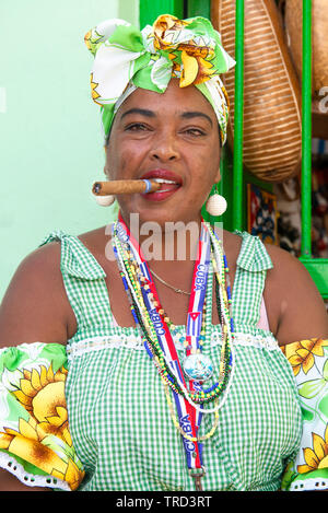 Colourfully dressed cuban lady sitting smoking a large cigar in one of the streets in the Old Town of Havana, Cuba, Caribbean Stock Photo