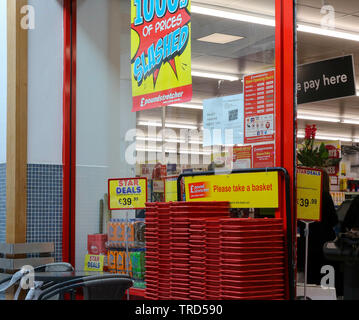 Red plastic shopping baskets outside the entrance of a Poundstretcher store with 'pay here' sign in background. Stock Photo