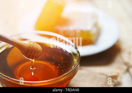 Honey dripping from wooden dipper honey jar and yellow sweet honeycomb slice background Stock Photo