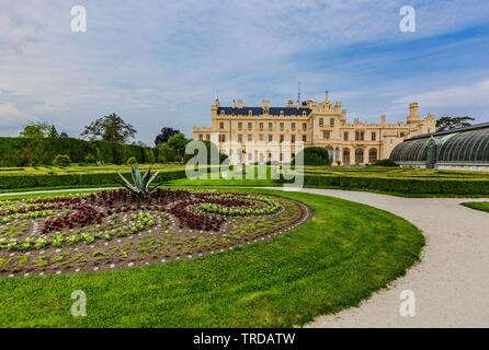 Lednice, Czech Republic - May 27 2019: Famous Lednice castle in South Moravia with yellow facade. Garden with green lawn, bush and flowers in foregrou Stock Photo