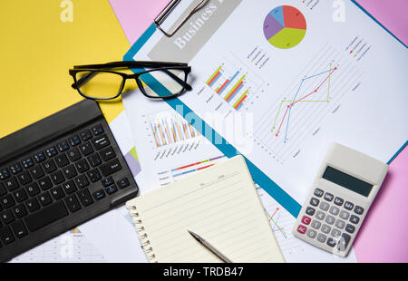 Financial and business graph chart report paper document with calculator open notebook paper pen glasses and keyboard on colorful background Stock Photo