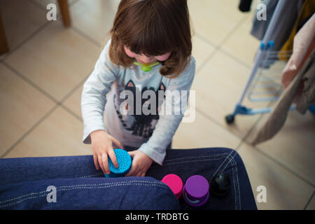 toddler baby girl with pacificator, playing at home with colorful vases on denim sofa. Top view, natural light. Stock Photo