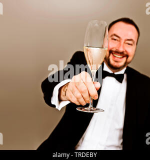 Portrait of an happy looking man dressed in dinner jacked holding a flute glass with champagne in his strechted out hand Stock Photo