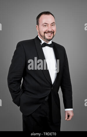 Portrait of a good looking and smiling man dressed in a smoking against grey background Stock Photo