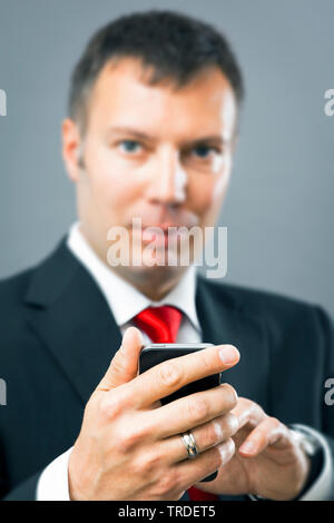 Portrait of a likeable smiling Businessman in a black suit using a smartphone against grey background Stock Photo