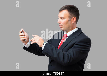 Portrait of a likeable Businessman in a black suit using a smartphone against grey background Stock Photo