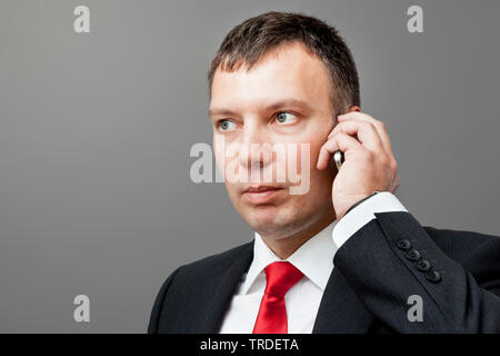 Portrait of a likeable Businessman in a black suit making a phone call against grey background Stock Photo