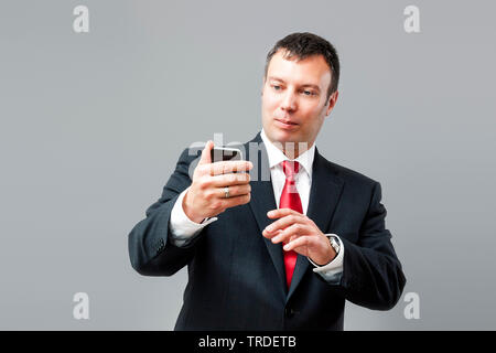Portrait of a likeable Businessman in a black suit looking at his smartphone against grey background Stock Photo
