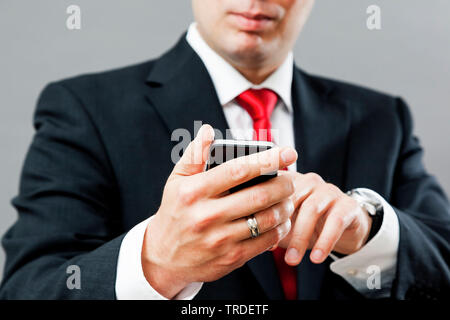 Portrait of a likeable Businessman in a black suit using a smartphone against grey background Stock Photo