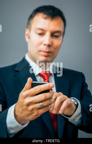 Portrait of a likeable Businessman in a black suit using a smartphone against grey background Stock Photo