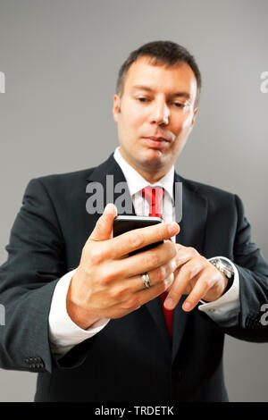 Portrait of a likeable Businessman in a black suit using a smartphone against grey background Stock Photo