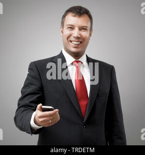 Portrait of a likeable smiling  Businessman in a black suit holding a smartphone against grey background Stock Photo