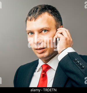 Portrait of a likeable Businessman in a black suit making a phone call against grey background Stock Photo