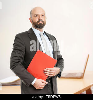 Portrait of a competent looking Businessman holding a red envelop in front of a desk Stock Photo