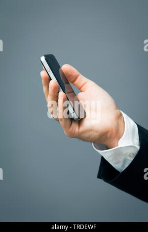 Close-up view of a hand with a black suit holding a smartphone against grey background Stock Photo