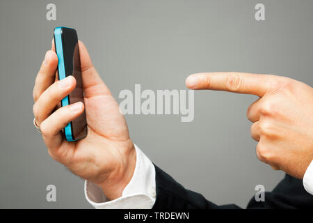 Close-up view of hands; one holding a smartphone and one pointing towards it Stock Photo