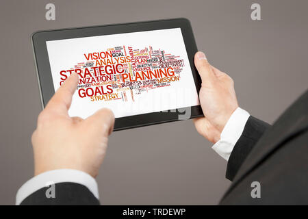 Close-up view of hands holding a tablet showing a tag cloud about strategy Stock Photo