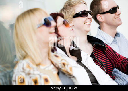 Group portrait/side view of 4 young persons wearing sunglasses sitting and smiling Stock Photo