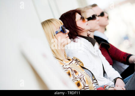 Group portrait/side view of 4 young persons wearing sunglasses sitting and looking to the right Stock Photo