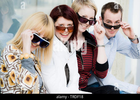 Group portrait/side view of 4 young persons wearing sunglasses sitting and looking into the camera Stock Photo