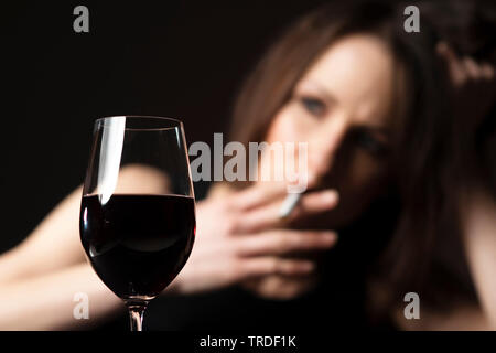 Portrait of a depressed and alcoholised woman smoking a cigarette with a glass of wine Stock Photo