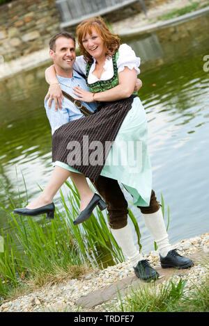 Portrait of a young couple dressed in traditional costumes in front of a pond, Germany, Bavaria Stock Photo