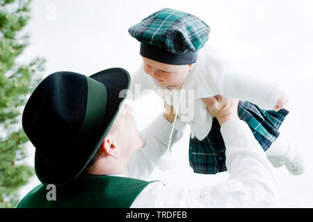 Portrait of a young man dressed in traditional costume holding up a baby, Germany, Bavaria Stock Photo