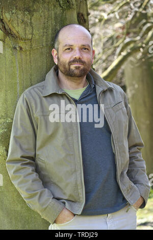 man leaning against a tree trunk, Germany Stock Photo