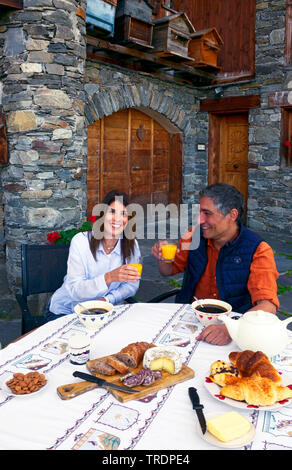 couple at the breakfast table in front of an old house, France, Savoie, Sainte Foy Tarentaise Stock Photo