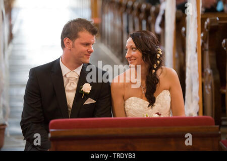 Bridal couple at the church sitting in front of the altar and gaze lovingly at each other Stock Photo