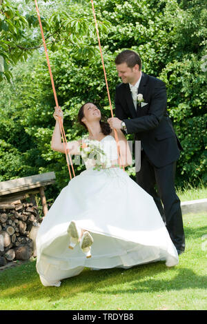 Wedding picture of a bride on a swing with the groom standing aside Stock Photo